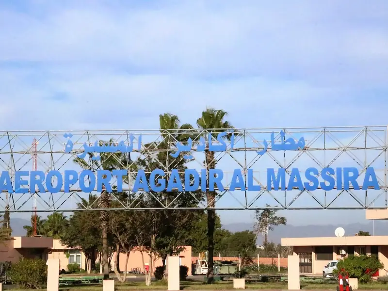 The entrance sign of Agadir Al Massira airport framed by palm trees